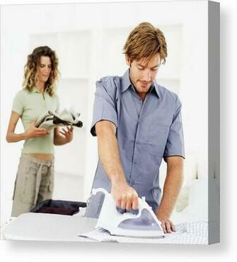 Young Man Ironing Clothes With A Woman Standing In The