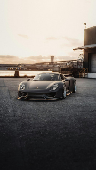 A Black Sports Car Parked On Road By Building And Water Photo