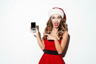 Smiling Young Woman In Santa Claus Hat Pointing Finger At Blank