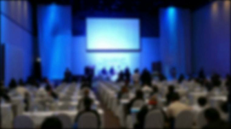 People Sit On Rows Of Chairs In Large Conference Convention Hall