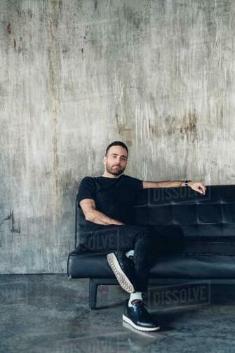 Man Sitting On Sofa Concrete Wall In Background Stock Photo