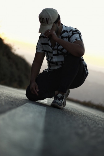 A Man Sitting On The Side Of Road Wearing Hat Photo