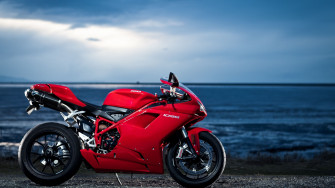 A Red Motorcycle Parked Next To The Ocean Wallpaper