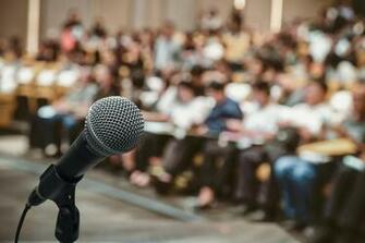 Microphone Over The Abstract Blurred Photo Of Conference Hall Or