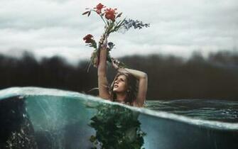 Woman Half Submerged In Water Holding Up A Red Flower