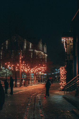 A Group Of People Walking On Sidewalk With Christmas Lights