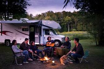 Family Gathered Around Campfire With Rv In Background