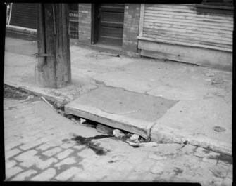 Sidewalk With Patched Pavement And Clogged Sewer Drain Store