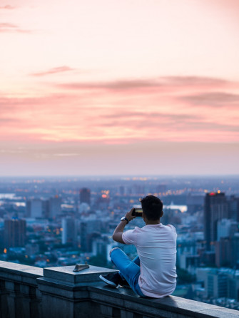 Person Sitting On Edge Of Building Taking Photo City During