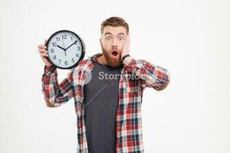Surprised Shocked Young Man In Plaid Shirt Holding Wall Clock Over