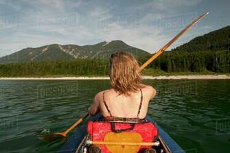 Rear Of Woman Paddling A Canoe With Mountain Range In