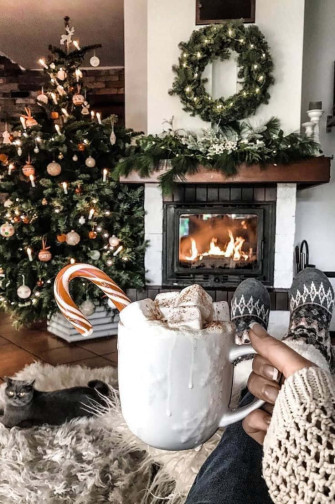 A Person Is Sitting In Front Of Fireplace With Cup