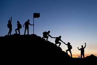 Silhouette Of People Helping Each Other Hike Up A Mountain At Sunset Background Wallpaper