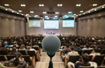Microphone Over The Abstract Blurred Photo Of Conference Hall Or