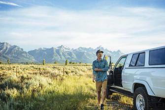 Young Man Walking By Car With Mountains In Background At Grand