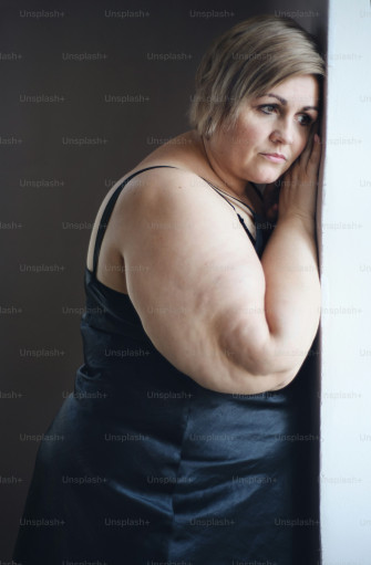 A Lonely Fat Woman Standing And Looking Through The Window At Home Wallpaper