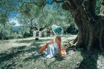 Young Woman With Straw Sun Hat Under An Olive Tree On A Background