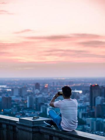 Person Sitting On Edge Of Building Taking Photo City During